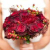 Winter-themed nosegay bouquet with dark red roses and berries
